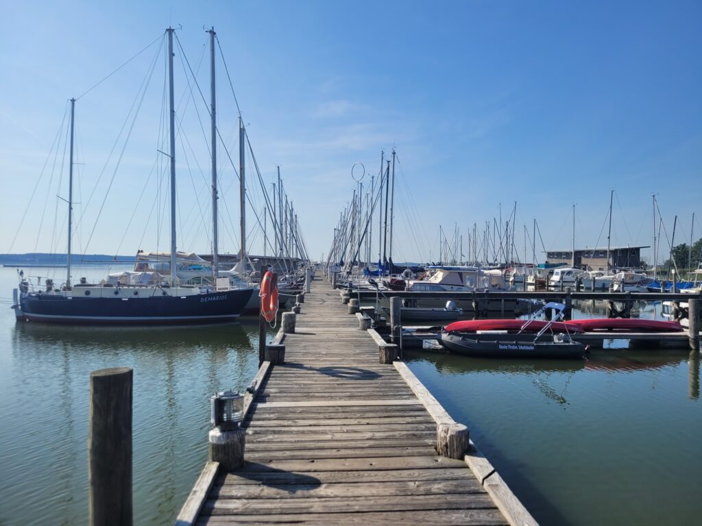 Holzsteg führt zwischen vertäuten Segel- und Motorbooten in ruhigem Hafen unter klarem blauem Himmel.