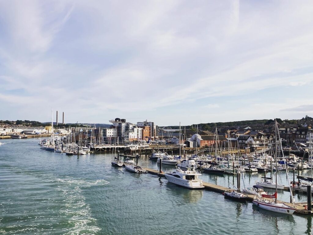 Marina mit dicht anliegenden Segelbooten und Yachten, angrenzende Kleinstadt, ruhiges Wasser unter blauem Himmel