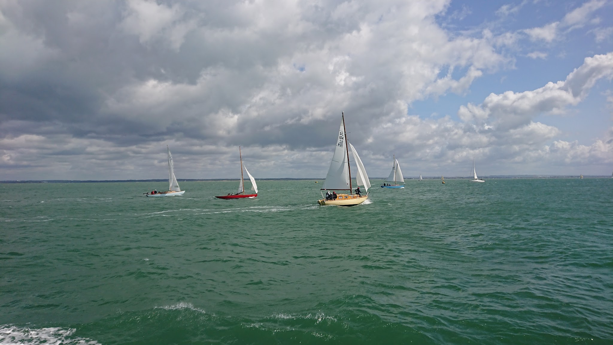 Mehrere Segelboote kreuzen auf grünem Meer unter teils dunklen, teils hellen Wolken.