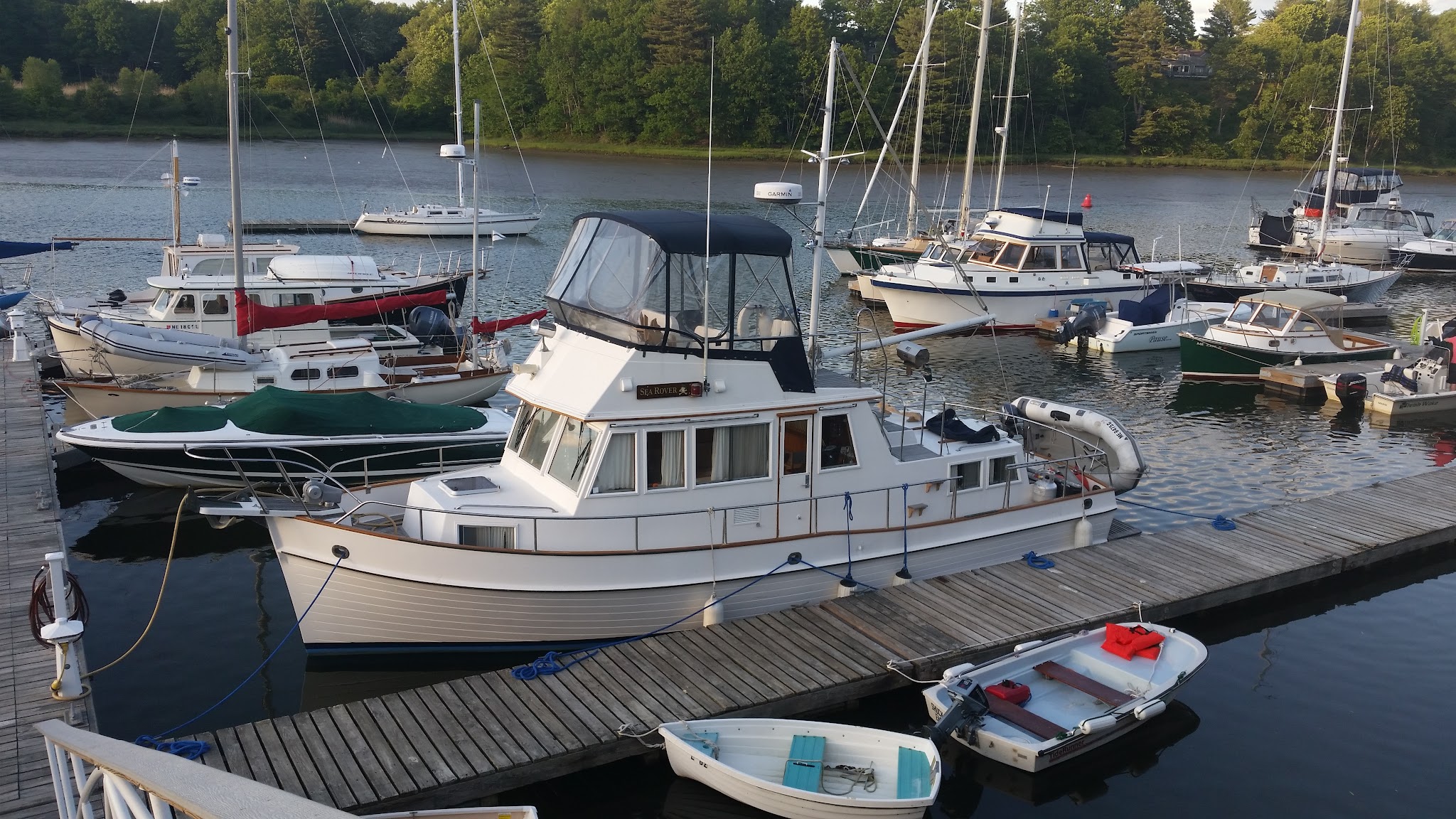 Mehrere Boote liegen an Holzstegen im ruhigen Hafen; im Mittelpunkt ein größerer weißer Kabinenkreuzer.