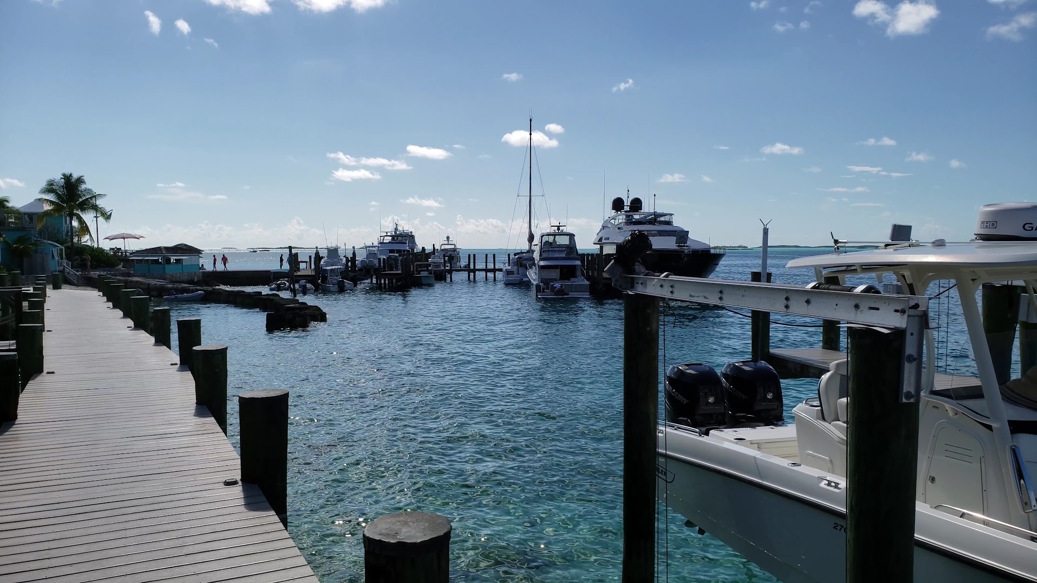 Holzsteg am türkisblauen Hafen, mehrere Yachten vertäut, Palmen und klarer Himmel erzeugen Urlaubsstimmung.