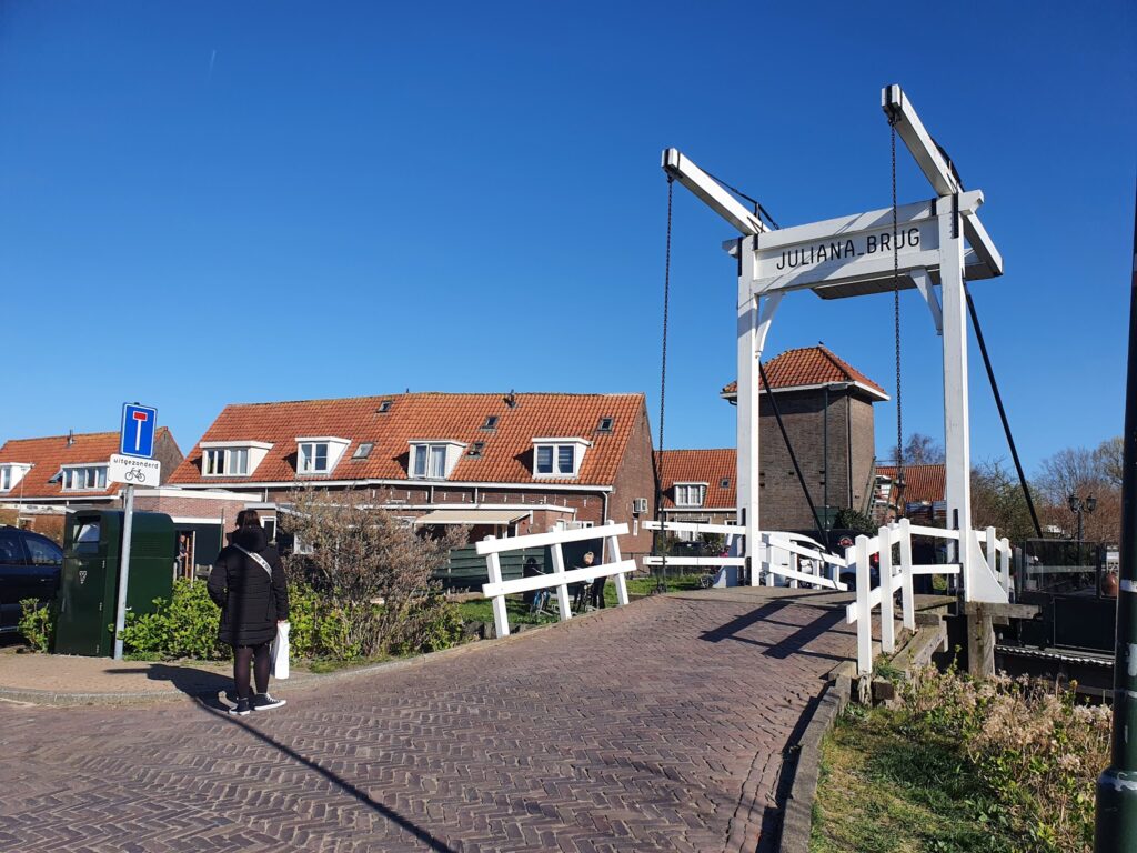 Weiße Zugbrücke „Juliana-brug“ vor roten Ziegeldächern, blauem Himmel; Person im Mantel nähert sich.
