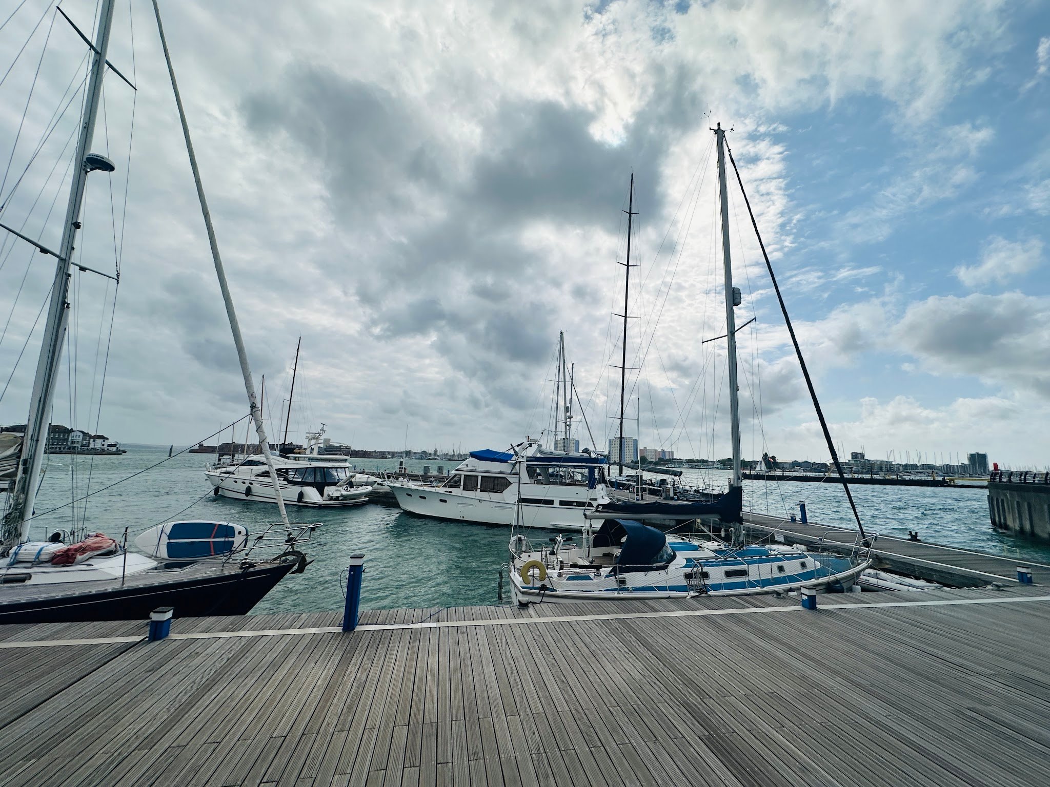 Mehrere Segel- und Motoryachten liegen an einem hölzernen Steg im Hafen unter bewölktem Himmel.