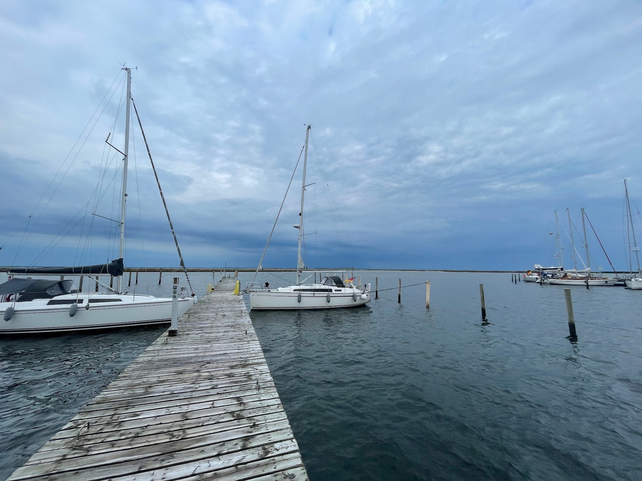 Holzsteg zu Segelbooten auf ruhigem Wasser unter bewölktem Himmel.