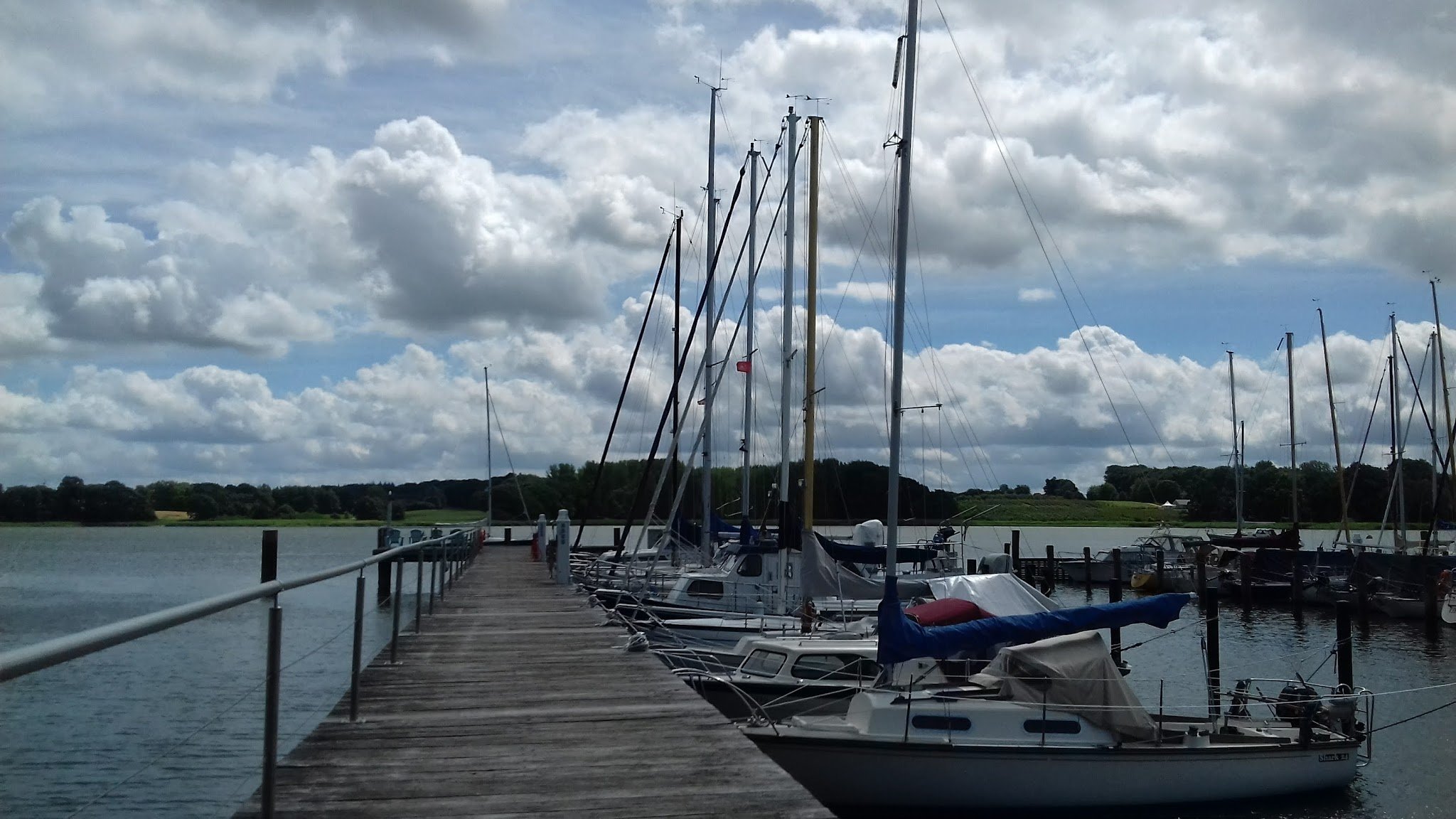 Steg mit festgemachten Segelbooten, ragt in ruhiges Wasser unter wolkigem Himmel