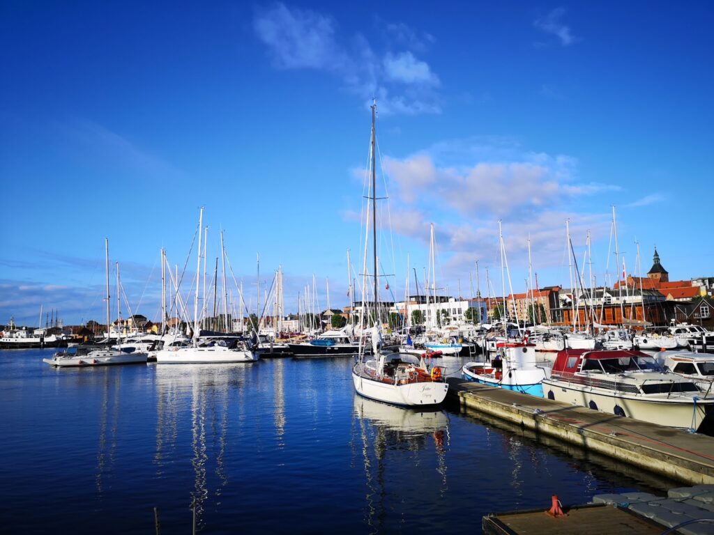 Yachthafen mit dicht aneinandergereihten Segelbooten, ruhiges Wasser reflektiert Masten unter blauem Himmel.