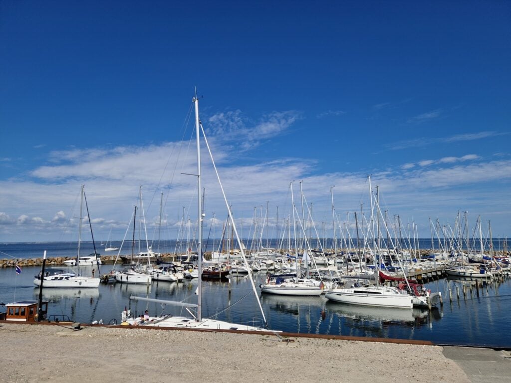 Yachthafen voller Segelboote unter strahlend blauem Himmel; ruhiges Wasser spiegelt Masten.