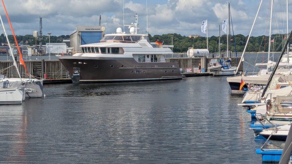 Große Motoryacht liegt im Hafen neben Segelbooten, ruhiges Wasser unter teils bewölktem Himmel.