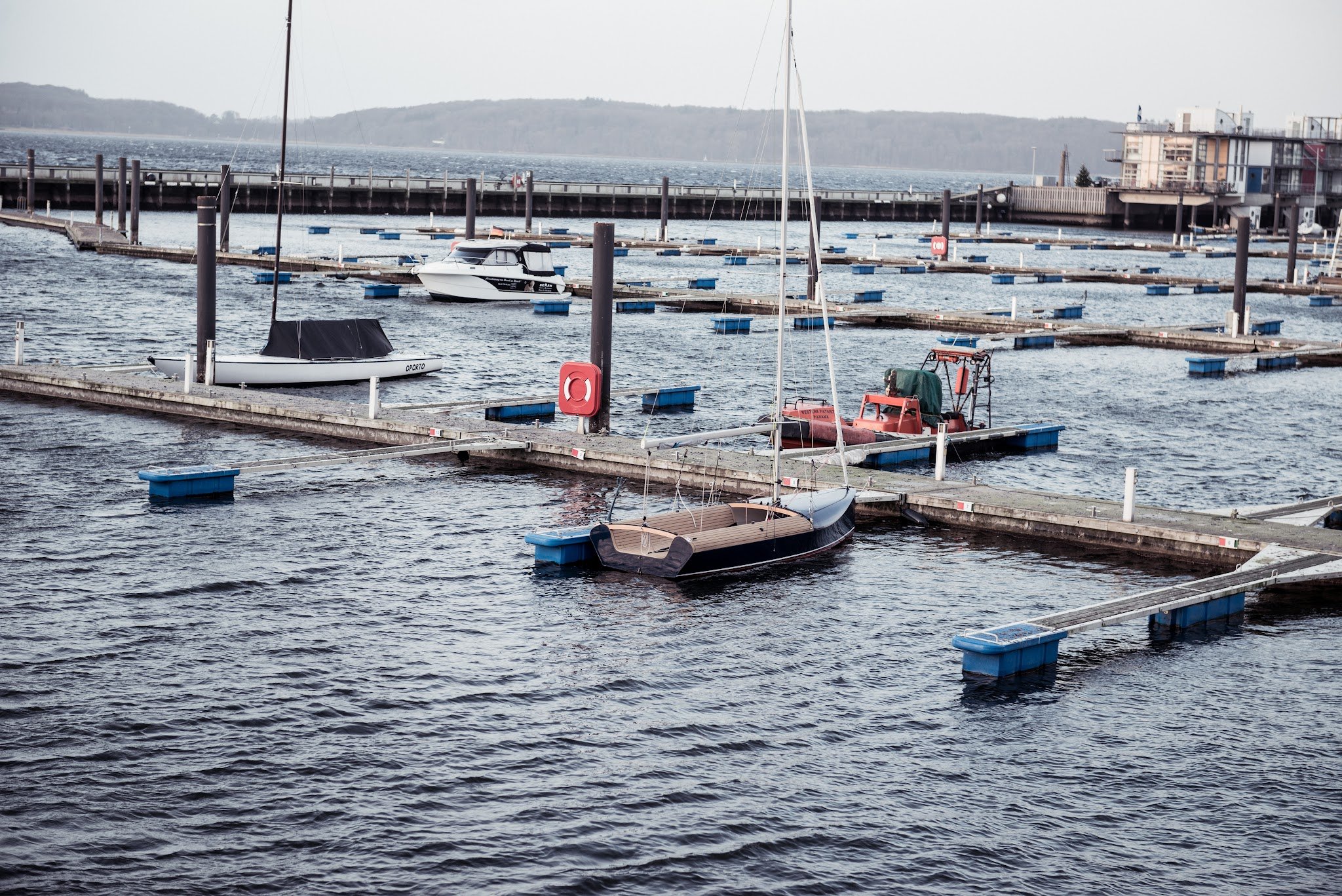 Fast leerer Jachthafen mit wenigen Booten an schwimmenden Stegen, dahinter ruhiges Wasser und bewaldete Küste.
